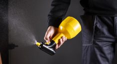 Close-up of a person using a yellow pest control sprayer to manage pests.
